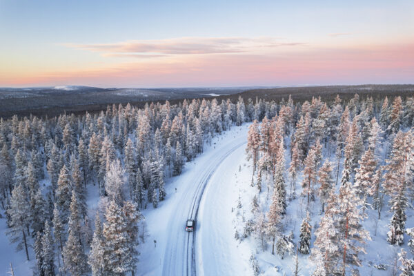 Car traveling icy mountain road across the frozen forest at sunrise, Yllas, Pallas-Yllastunturi National Park, Finnish Lapland, Finland