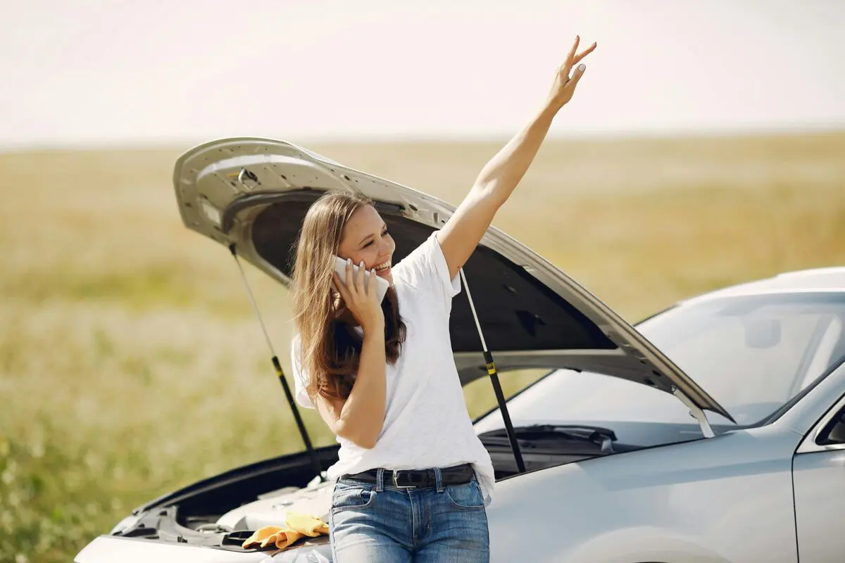 Smiling woman sitting on the front of her car with the hood open representing cross border motor claims assistance by Van Ameyde
